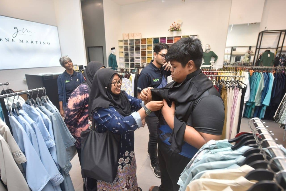 Siti Mariam (kiri) menyarungkan baju Melayu kepada adiknya yang masih bersekolah.