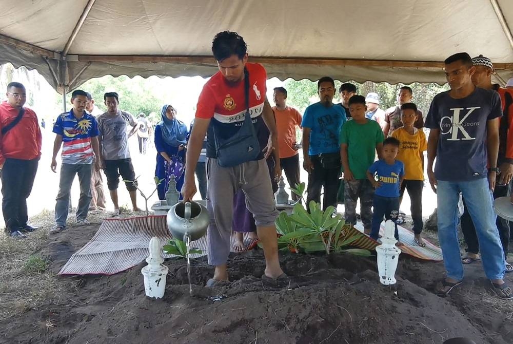 Muhammad Ubaidillah Zikri menyiram pusara anak sulungnya dan bapa mentua ketika pengebumian jenazah di Tanah Perkuburan Padang Polis Batu Rakit, di Kuala Nerus pada Selasa.