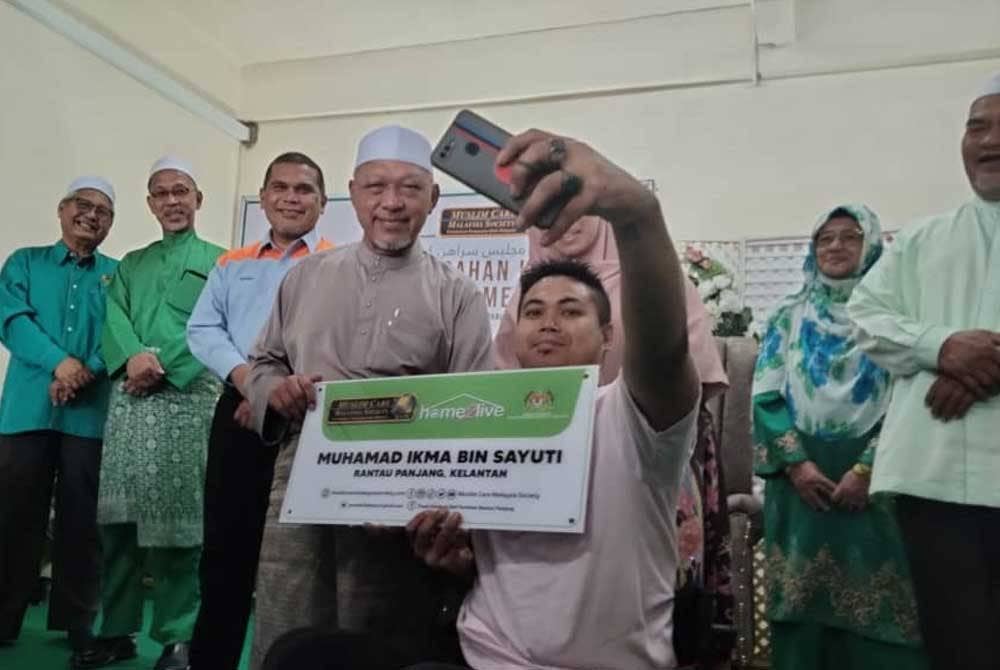 Mohamad Ikma mengambil peluang berswafoto bersama Ahmad ketika menyerahkan kunci rumah pada Majlis Serahan Kunci 10 Rumah 'Home2Live' di Pusat Latihan dan Aktiviti Komuniti Rantau Panjang pada Rabu.