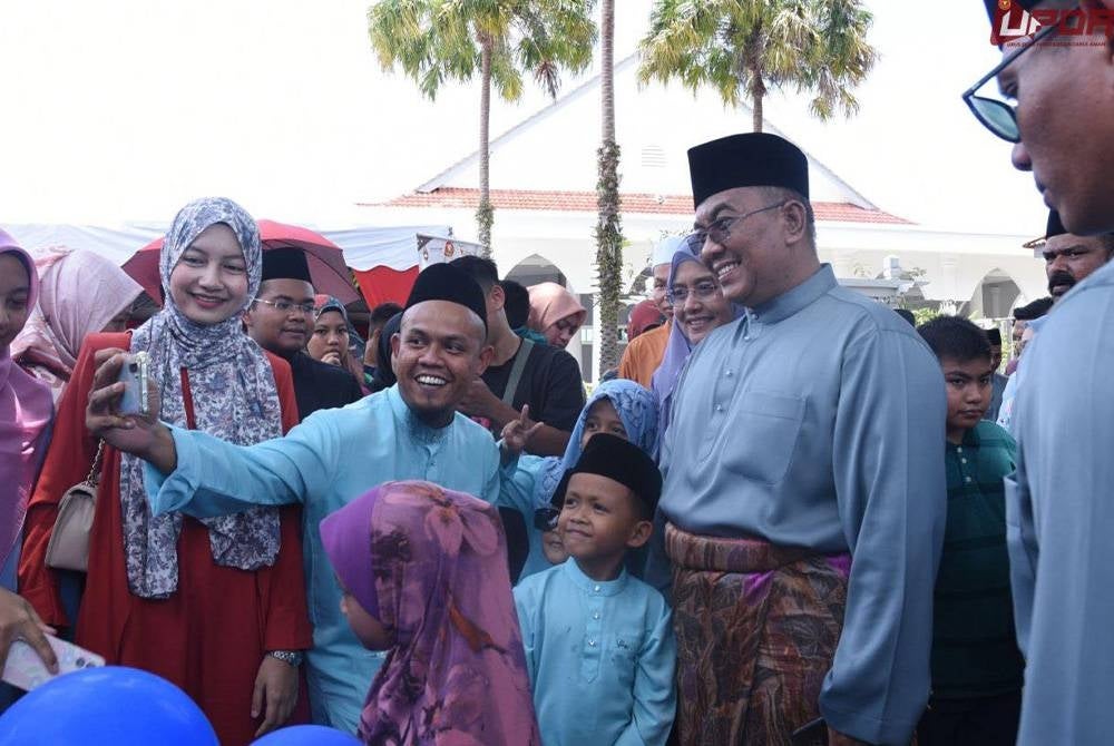 Muhammad Sanusi (kanan) melayan tetamu yang hadir untuk berswafoto sempena Rumah Terbuka Aidilfitri di Seri Mentaloon.