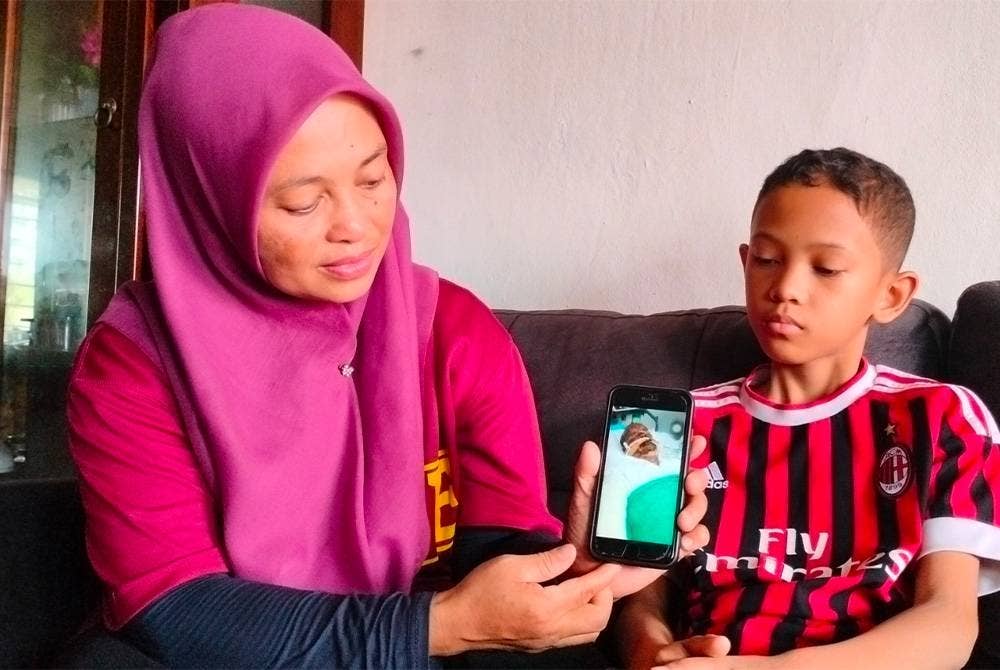 Zarni Yuherlina bersama anak ketiganya menunjukkan gambar suaminya yang sedang menerima rawatan di hospital.