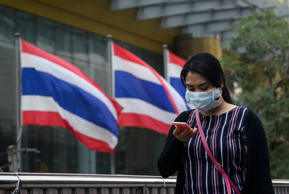 Une femme porte un masque facial en se promenant à Bangkok.  -AFP