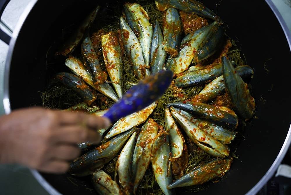 Zainab menyusun ikan selayang di atas daun asam gelugur ketika melakukan proses penghasilan gulai kering daun asam gelugur. - Foto: Bernama