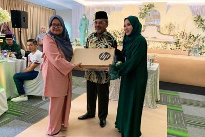 Tajuddin (tengah) bersama Tina (kanan) menyampaikan set komputer riba kepada pelajar TIC sempena majlis Rumah Terbuka Aidilfitri TT Group Companies pada Ahad.