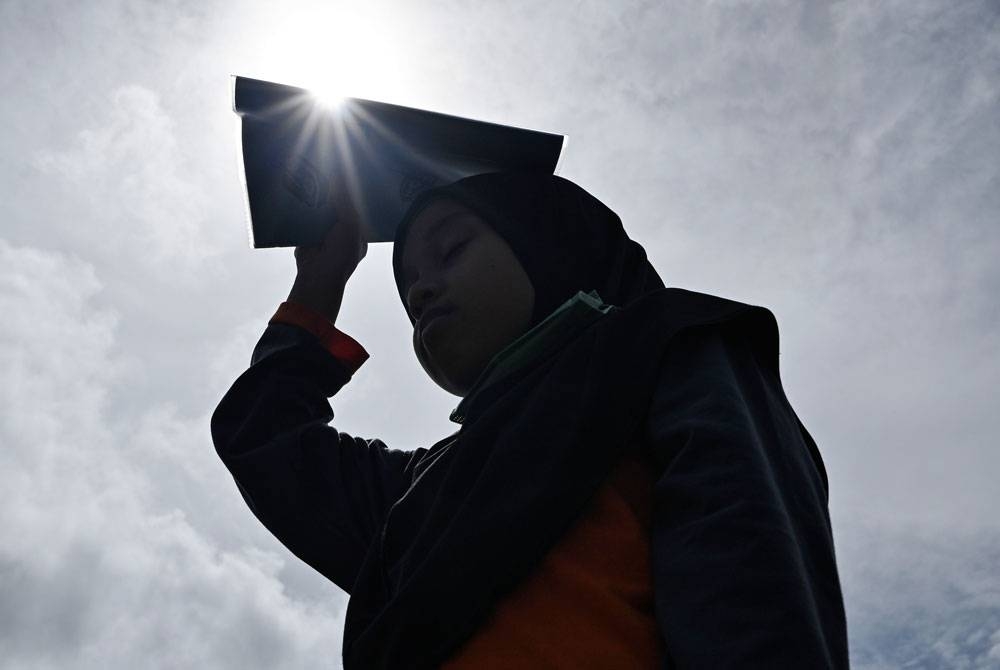 Seorang murid sekolah menutup kepala dengan buku susulan cuaca panas.
