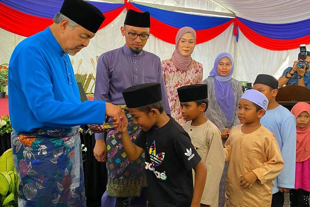 Ahmad Zahid menyampaikan duit raya kepada kanak-kanak semasa Majlis Mesra Aidilfitri Felcra Berhad di Bukit Tiu, Machang pada Sabtu.