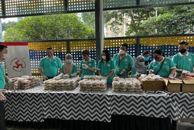 Kakitangan jenama Cap Kaki Tiga membantu mengagihkan makanan.