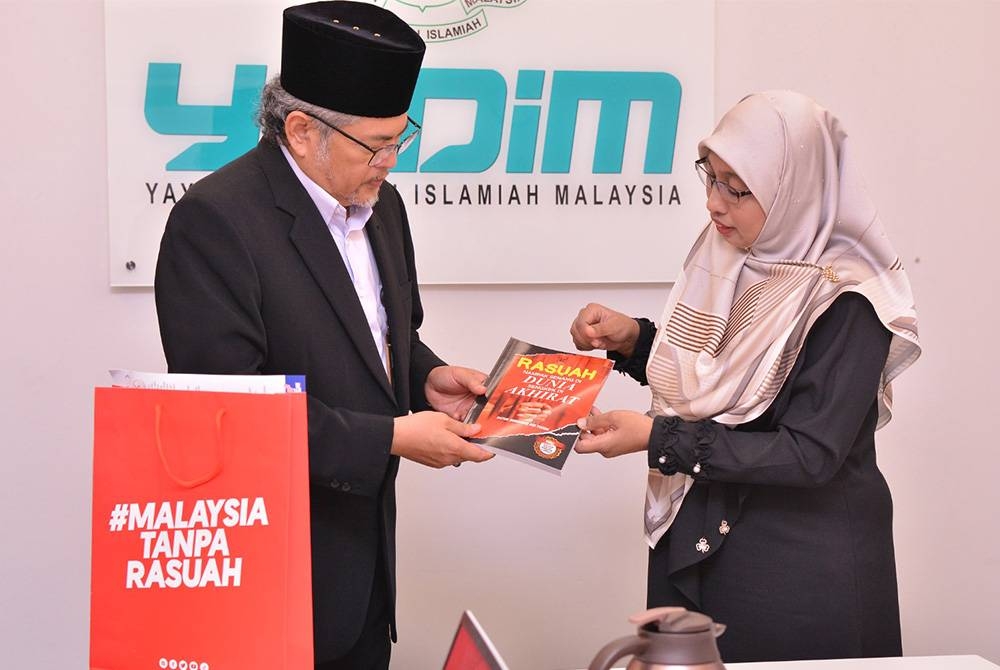 Nurhayati Nordin menyerahkan buku berjudul Rasuah Nampak Senang di Dunia, Sengkek di Akhirat kepada Hasanuddin Mohd Yunus selepas usai sesi perbincangan.