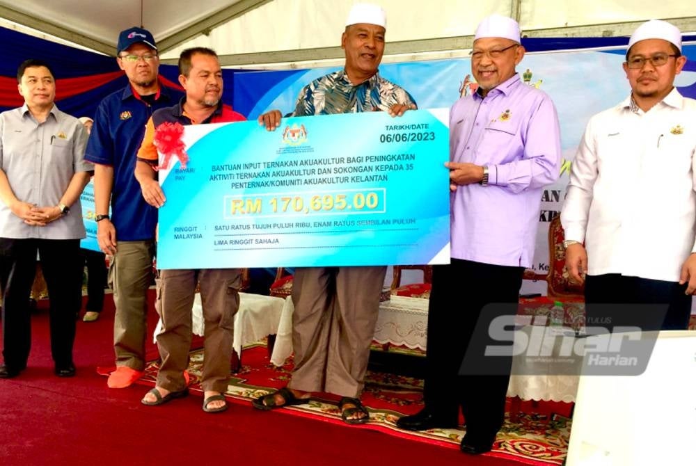 Ahmad (dua dari kanan) diiringi Adnan (dua dari kiri) menyampaikan bantuan input ternakan akuakultur kepada penternak ikan di Pasir Puteh.