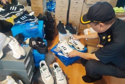 Pegawai KPDN memeriksa kasut dipercayai tiruan selepas menyerbu sebuah rumah di Taman Chai Leng, Perai pada Khamis.