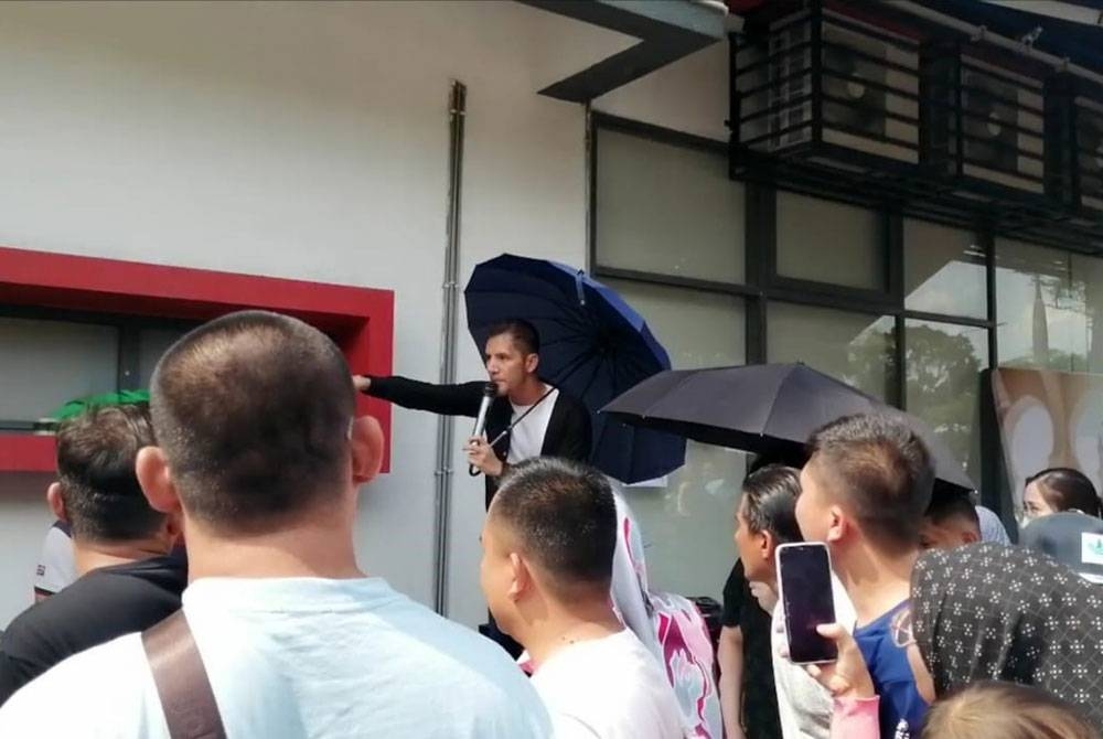 Aliff Syukri berpayung sambil menjual durian di Wisma D'Herbs pada Ahad.