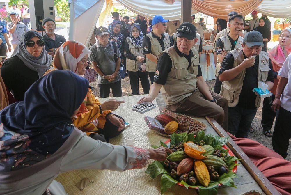 Fadillah (duduk, kanan) beramah mesra bersama penduduk ketika melawat ruang pameran berkaitan tanaman koko.