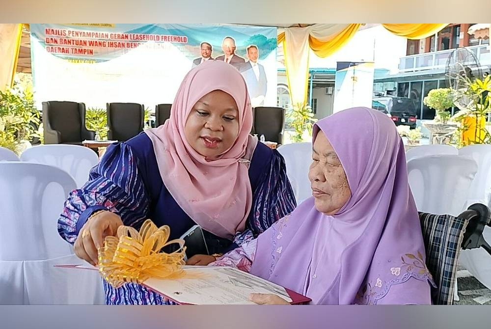 Siti Khadijah @ Normah Maamor, 83 (kanan) bersama anaknya melihat geran yang diterima mereka pada majlis berkenaan.