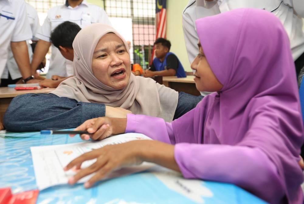 Fadhlina (kiri) bertanyakan sesuatu kepada Najwa Zulkifli semasa membuat lawatan ke Kelas Tingkatan 1 K9 Arus Perdana dan Program pendidikan Khas Integrasi (PPKI) sempena perasmian Sekolah Kebangsaan Pulau Beluru sebagai Sekolah Komprehensif 9 di Kampung Pulau Beluru, Palekbang Tumpat pada Khamis. - Foto Bernama