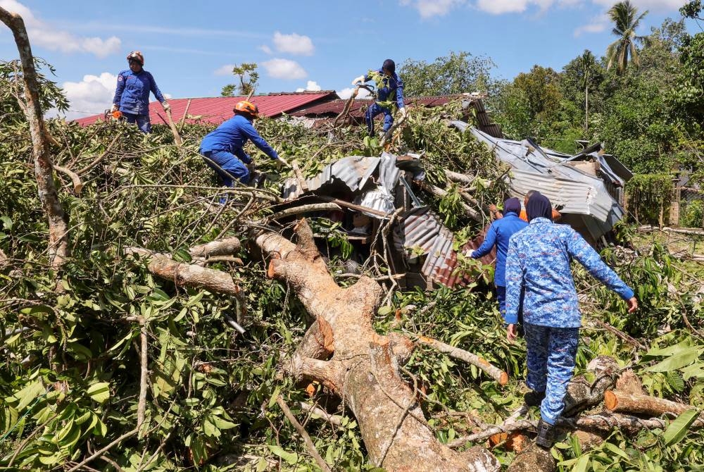 Anggota Jabatan Angkatan Pertahanan Awam Malaysia (JPAM) Pasir Puteh membantu membersihkan rumah yang dilanda ribut di Kampung Permatang Sungkai. - Foto Bernama