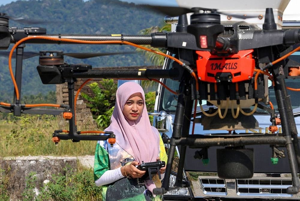 Siti Hajar menerbangkan dron bagi kerja-kerja menyembur racun untuk tanaman padi di Kampong Lepah Selising. -Foto Bernama