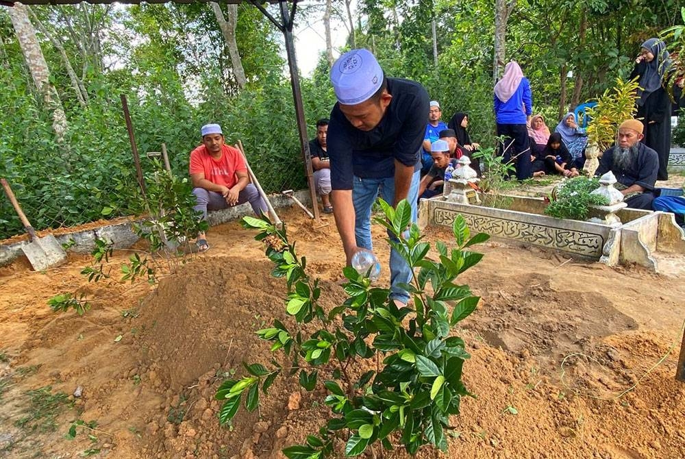 Anak lelaki arwah, Muhamad Ariffin, 30, memberi penghormatan terakhir pada arwah bapanya di Tanah Perkuburan Islam Mukim Telosan.
