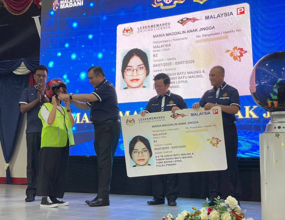 Anthony (tiga dari kiri) memakaikan topi keledar kepada salah seorang penerima dalam Majlis Penyerahan Lesen Memandu di bawah program MyLesen B2 di Pusat Latihan Memandu Balik Pulau pada Sabtu.
