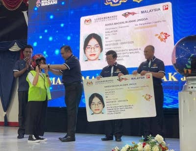 Anthony (tiga dari kiri) memakaikan topi keledar kepada salah seorang penerima dalam Majlis Penyerahan Lesen Memandu di bawah program MyLesen B2 di Pusat Latihan Memandu Balik Pulau pada Sabtu.
