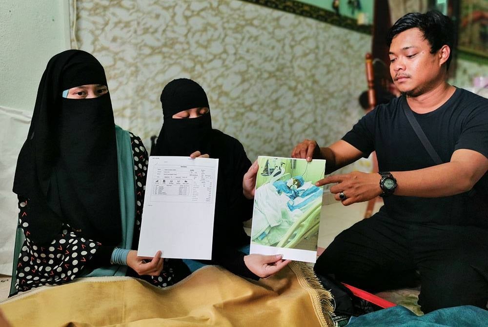 Zuraini (tengah) menunjukkan gambar ibu mereka ketika dirawat dan ditidurkan selama 40 hari di hospital swasta di Madinah ketika ditemui pemberita di rumah mereka di Taman Permint Jaya, Chendering di Kuala Terengganu.
