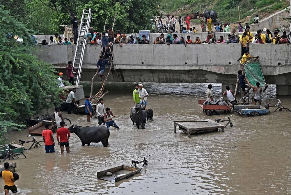 Orang ramai alih barang-barang mereka ke tempat selamat di jambatan Sungai Yamuna selepas hujan monsun lebat di New Delhi pada Rabu. - Foto AFP