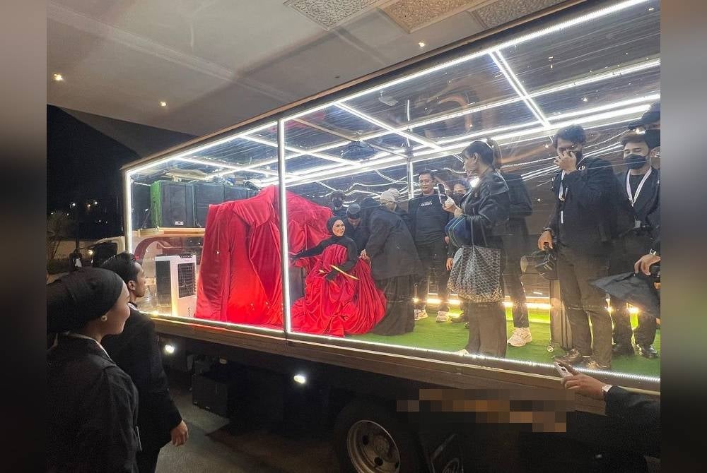 Aina hadir menaiki lori lut sinar dan turun di hadapan pintu utama dengan mengenakan blazer saiz gergasi berona merah. - Foto TV3