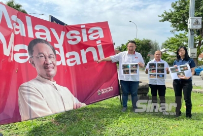 Andrew (kiri) menunjukkan salah satu papan iklan 'Malaysia Madani' yang sudah senget di kawasan Bukit Jambul.