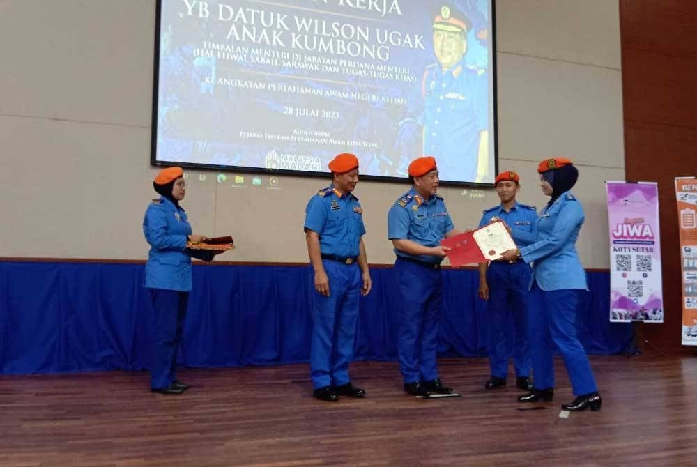 Wilson Ugak (tengah) menyerahkan Sijil Riben Pertahanan Awam kepada anggota APM ketika lawatan kerja beliau ke APM Kedah di PDPA Kota Setar pada Jumaat.