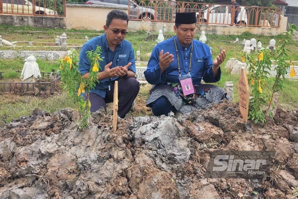 Mohd Zamri (kanan) menziarahi kubur bapanya di Tanah Perkuburan Islam Ar Raudhah Pekan Tanjong Karang pada Sabtu.