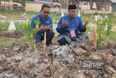 Mohd Zamri (kanan) menziarahi kubur bapanya di Tanah Perkuburan Islam Ar Raudhah Pekan Tanjong Karang pada Sabtu.