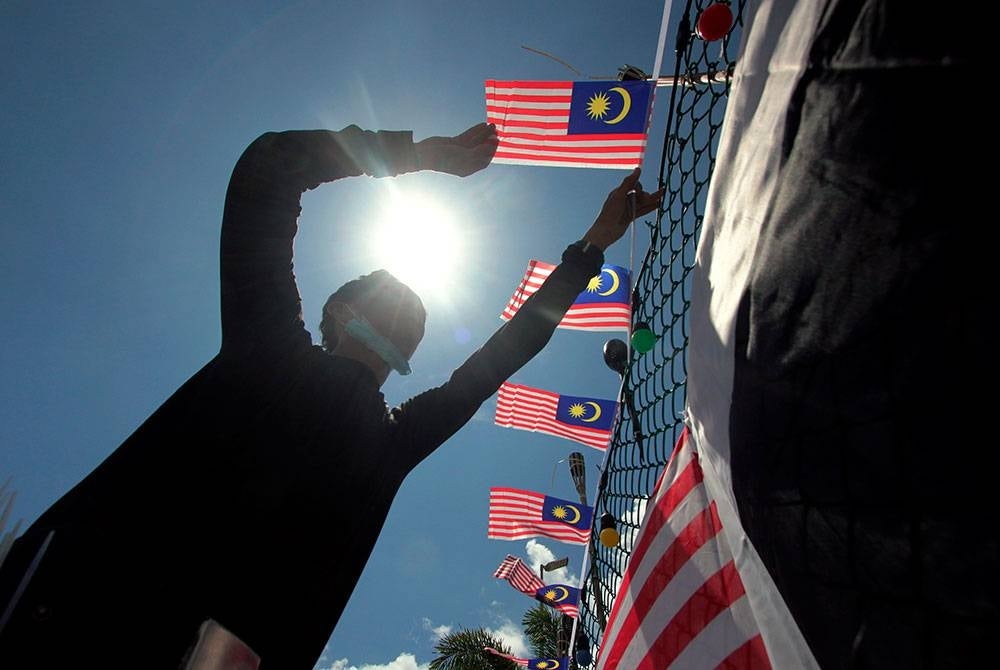 Pekerja sebuah pasar raya, Irwan Sudirman memasang Jalur Gemilang dan bendera Pahang pada pagar premis itu pada Sabtu. - Foto Bernama