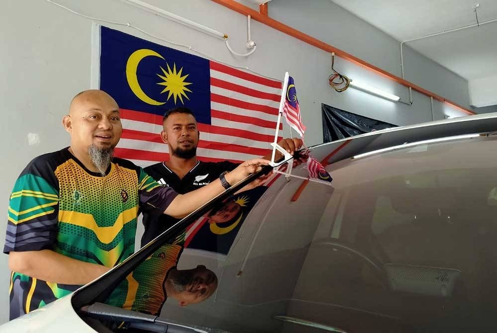 Abdul Salim (kiri) melekatkan Jalur Gemilang pada kenderaan salah seorang pelanggannya di Pusat Cucian Kenderaan Kazoku di Pekan Razaki di sini pada Ahad.