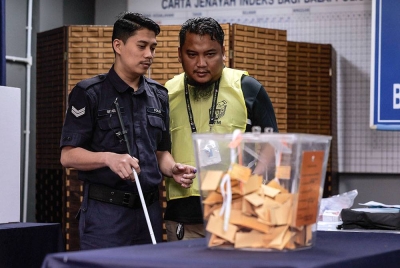 Anggota Polis Diraja Malaysia Koperal Abdullah Sidee Mohamed, 35, yang cacat penglihatan dibantu petugas Suruhanjaya Pilihan Raya (SPR) ketika proses pengundian awal sempena Pilihan Raya Negeri (PRN) Selangor di Ibu Pejabat Polis Daerah Kuala Selangor hari ini.