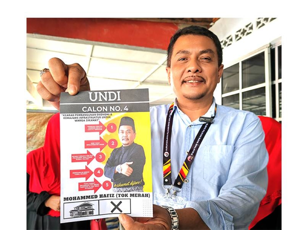 Mohammed Hafiz menunjukkan risalah yang menyenaraikan visinya kepada pengundi DUN Sikamat.