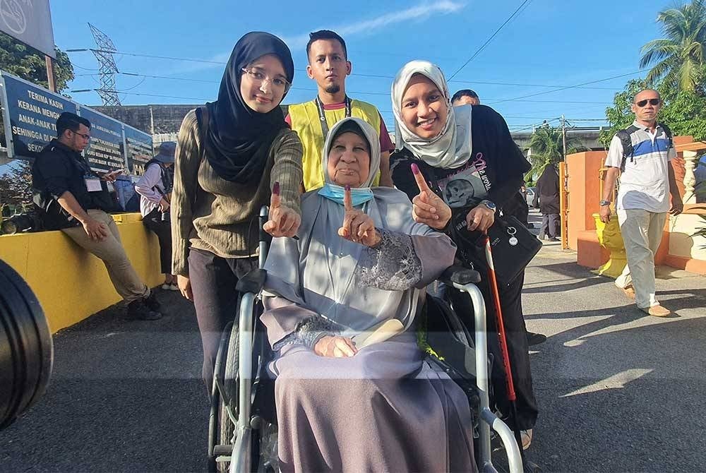 Siti Zainab (duduk) bersama cucunya, Faeah Afifah (kiri) dan Anis Nabilah (kanan) menunjukkan jari mereka menandakan telah selesai mengundi.