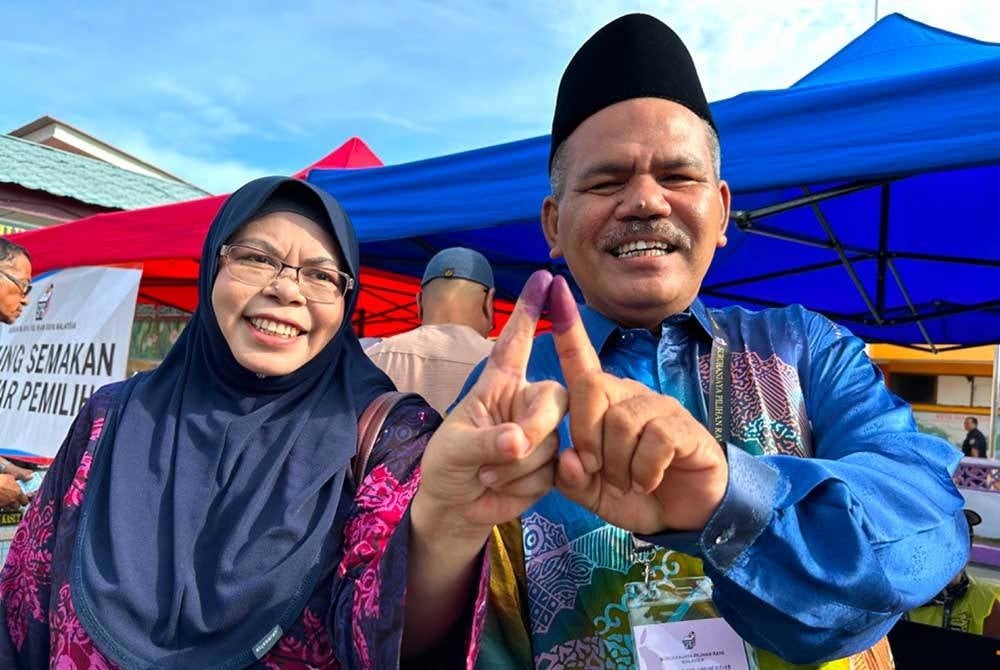 Ahmad (kanan) dan Nor Azma (kiri) menunjukkan jari berdakwat masing-masing selepas selesai mengundi pada Sabtu.