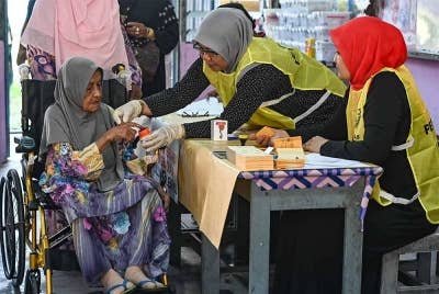 Warga emas, Aminah Othman, 96, (berkerusi roda) mencelup jari ke dalam bekas dakwat semasa mengundi bagi Dewan Undangan Negeri (DUN) Ru Rendang sempena PRN di Pusat Mengundi Sekolah Kebangsaan Rusila hari ini. - Foto Bernama