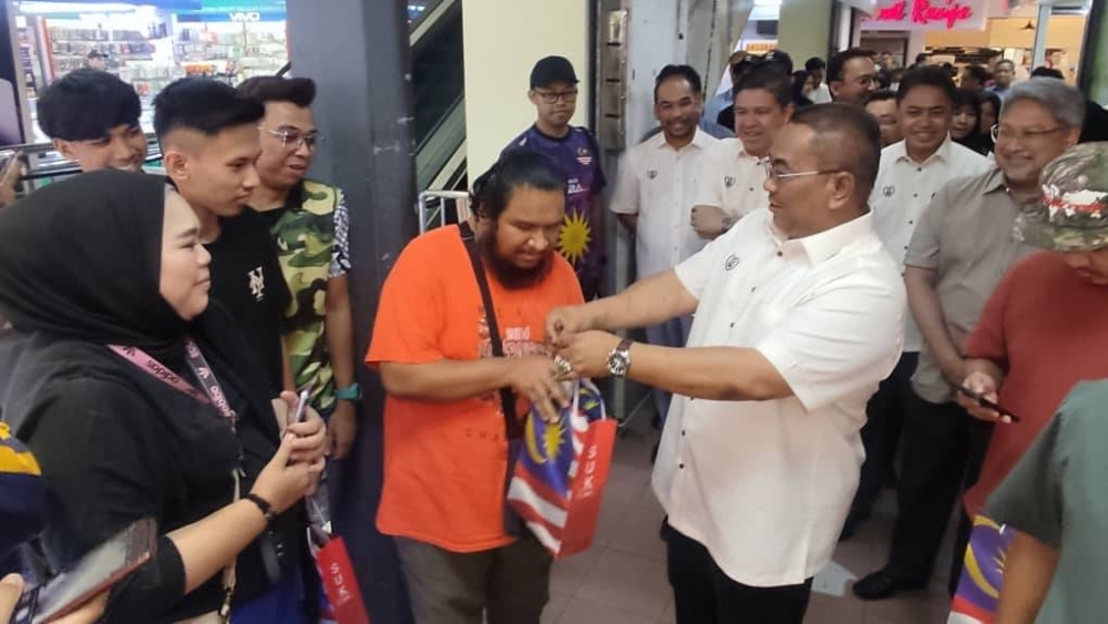 Muhammad Sanusi menyerahkan jalur gemilang kepada seorang pengunjung sempena Program Kempen Kibar Jalur Gemilang Peringkat Negeri Kedah di sebuah pasar raya, Alor Setar pada Selasa.