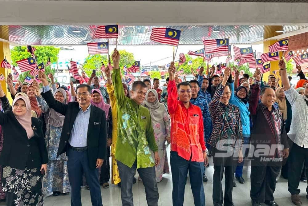 Dr Zaini (tiga dari kiri) dan Muhd Nor Aswadi (tengah) bersama kakitangan awam mengibarkan Jalur Gemilang di pekarangan Wisma Persekutuan di Kota Bharu pada Khamis.