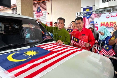 Muhd Nor Aswadi (tengah) yang mengiringi Dr Zaini melekatkan bendera Malaysia pada kenderaan di Wisma Persekutuan di Kota Bharu pada Khamis.