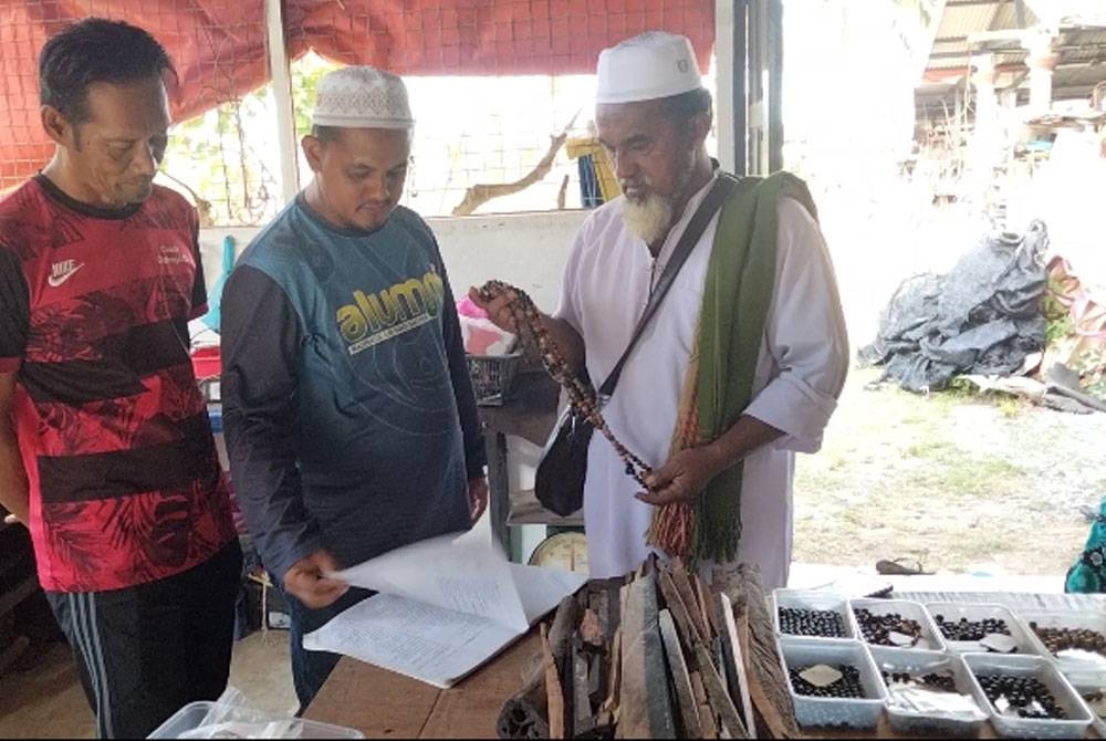 Ahmad Lokman (tengah) dan Roslan (kanan) meneliti buku senarai nama kayu untuk dicantumkan menjadi tasbih.
