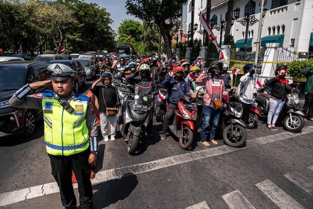 Polis trafik dan pengguna jalan raya memberikan tabik hormat ketika bendera Indonesia dikibarkan di Surabaya.