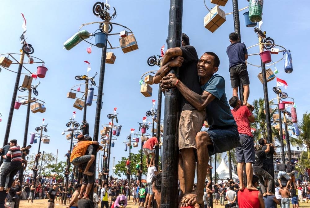 Peserta bertungkus lumus memanjat tiang yang disapu gris bagi mengambil hadiah di puncaknya semasa sambutan Hari Kemerdekaan di Pantai Ancol, Jakarta.
