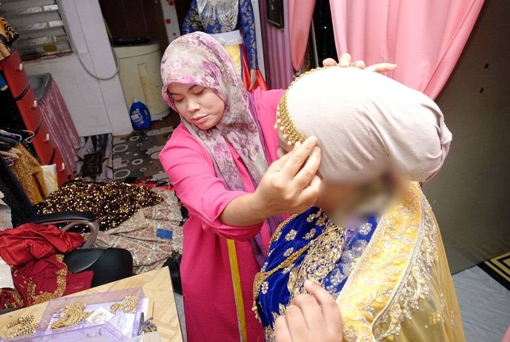 Rejamaiyah sedang melayan pelanggannya yang datang untuk menyewa pakaian di Bukit Katil di sini, pada Sabtu.