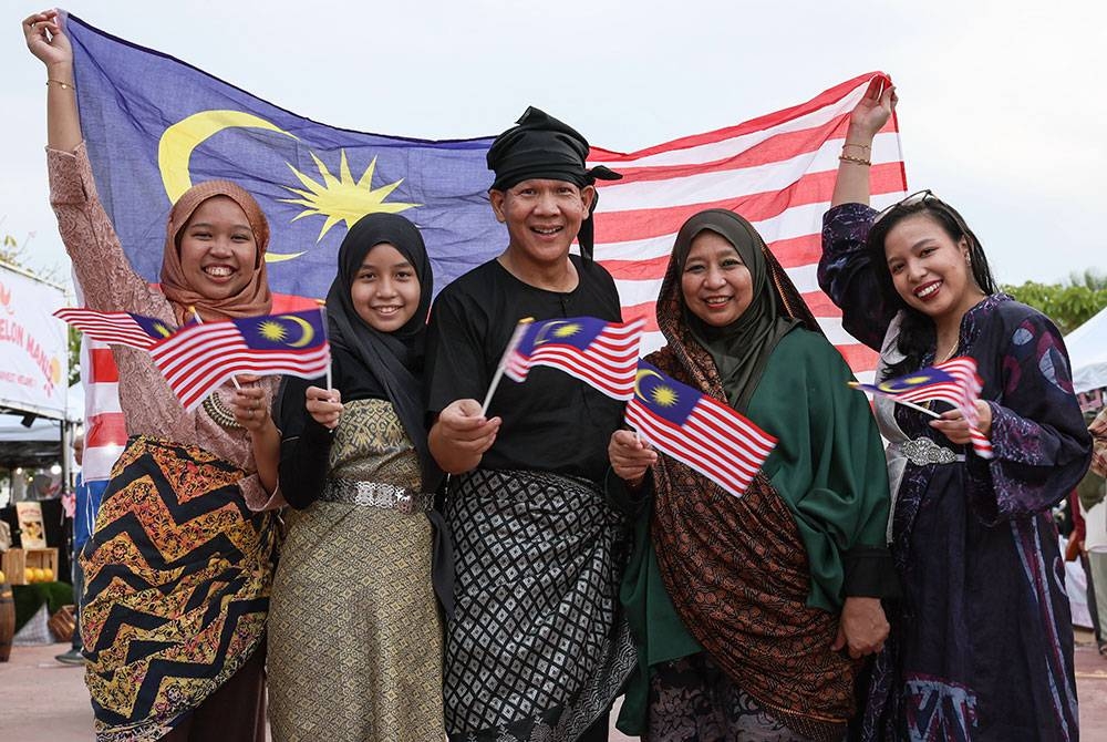 Peniaga, Wan D'zlyshah Wan Shahreman (tengah) bersama isteri Tengku Nurul Hidayah Tengku Abdul Malek (dua, kanan) serta anak-anak mereka yang berbusana tradisional Melayu mengibarkan Jalur Gemilang bagi menyemarakkan lagi sambutan Hari Kebangsaan 2023 semasa tinjauan di Payang Walk.