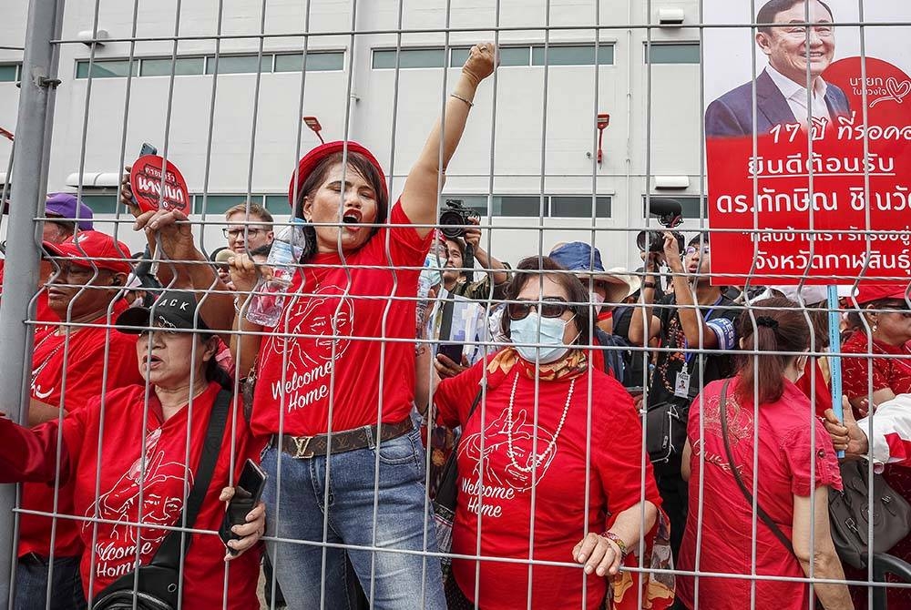 penyokong Thaksin berbaju merah berkumpul di luar terminal Lapangan Terbang Antarabangsa Don Muang bagi mengalu-alukan kepulangannya sambil memegang sepanduk. Foto EPA