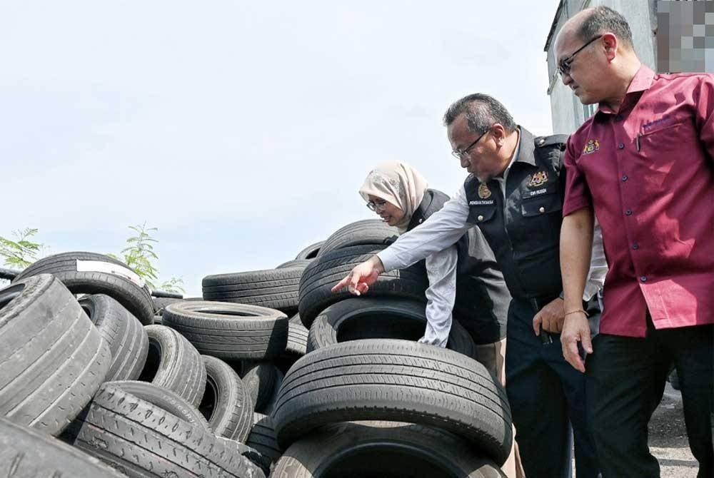 Hee Sam (kanan) melihat pelbagai saiz tayar dilonggokkan di kawasan terbuka oleh pemilik kedai tayar ketika operasi khas Op Tayar