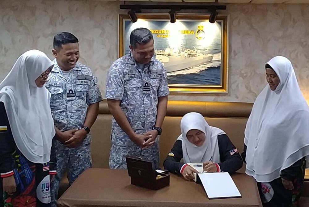 Maziah (duduk) menandatangani buku lawatan di dalam KD Teguh Samudera selepas program Malaysia #QuranHour.