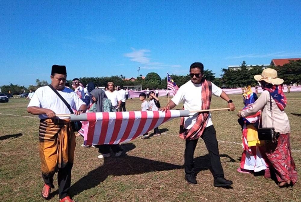 Kakitangan UMK membuka gulungan bendera sepanjang lebih 200 meter di Pusat Sukan UMK.
