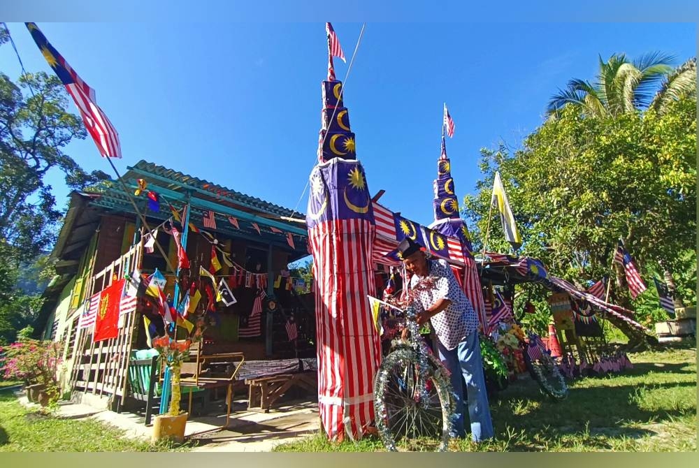 Mohd Kamil di hadapan rumahnya di Kampung Chulek yang dihiasi Jalur Gemilang dengan kreatif sempena program Halaman Rumah Merdeka.